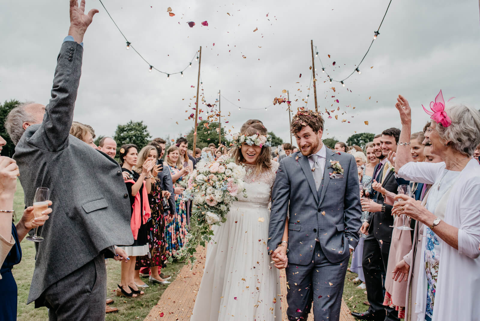 Bride wearing floral crown and groom passing through confetti gauntlet on their way to Shropshire tipi wedding reception