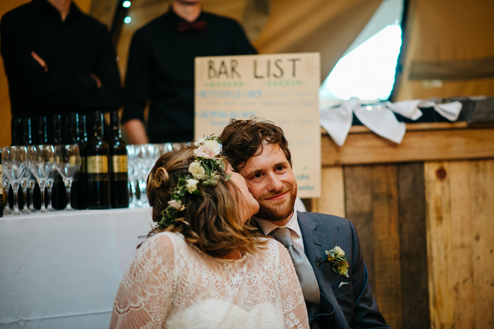 Bride lovingly kisses groom during speeches in tipi at Shropshire festival wedding