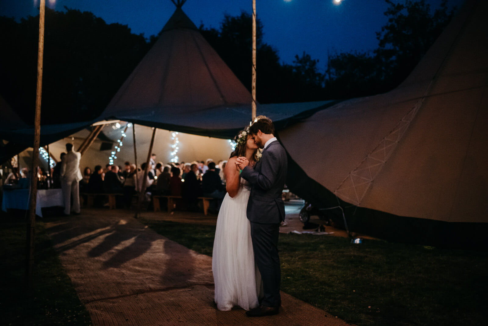 Bride and groom dancing in darkness with light coming from tipi and festoon lighting