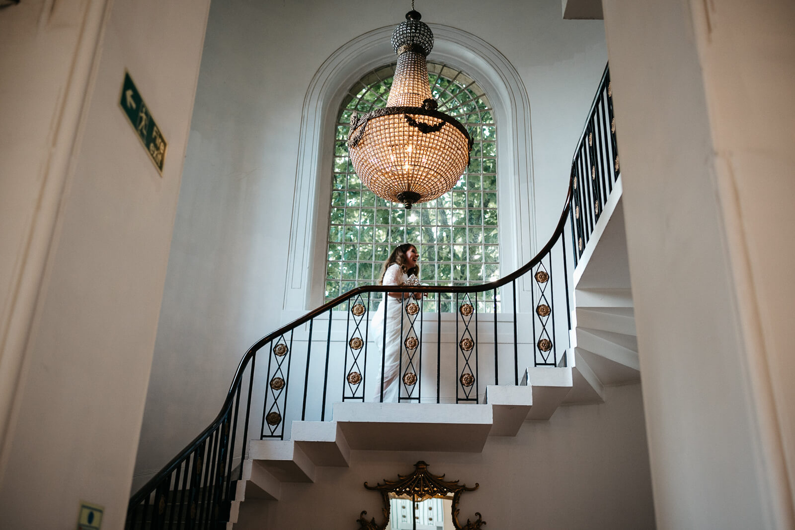 bride walks up elegant staircase under chandileir at London venue Marylebone One