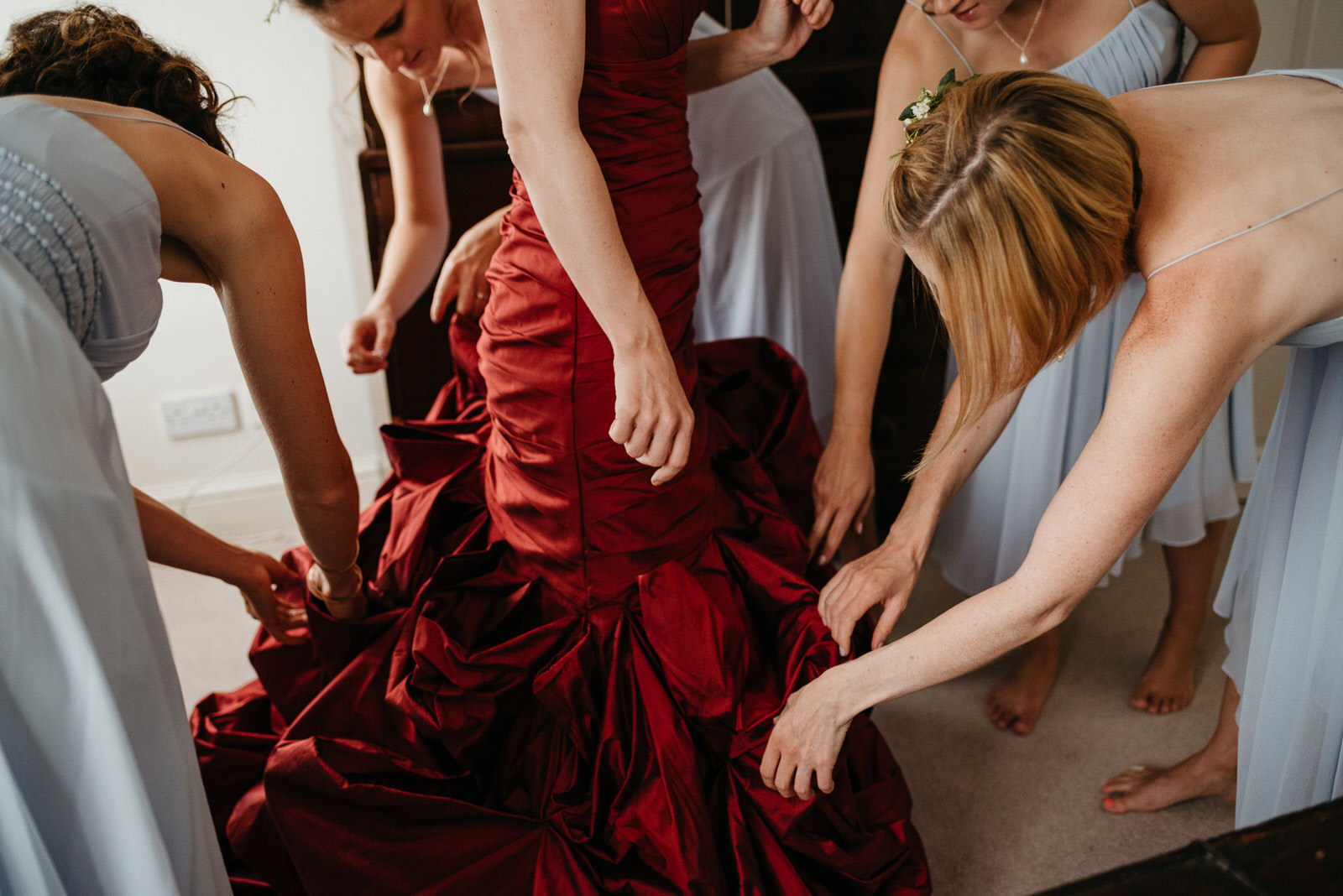 bridesmaids fuss with red taffeta wedding dress during morning getting ready