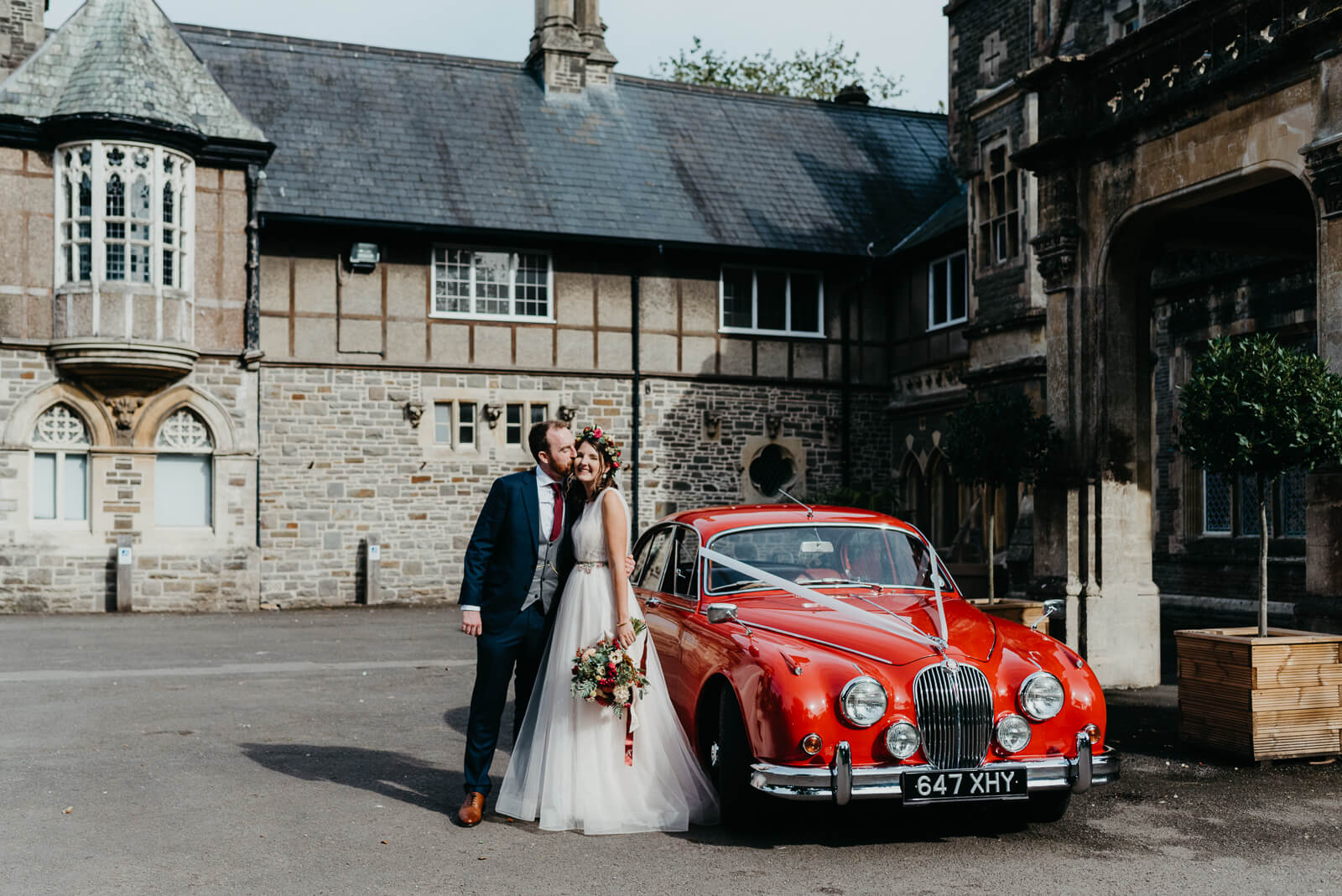 Bride and groom with red MKII Jaguar outside the main entrance of Insole Court wedding venue