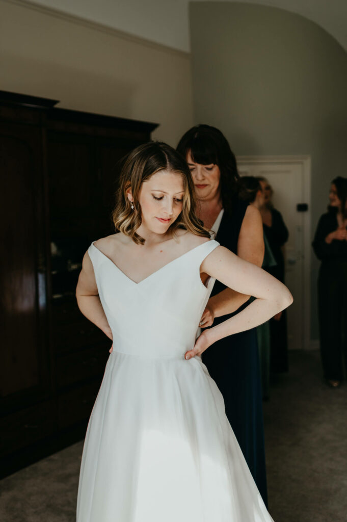 mother of the bride helps her daughter into her wedding dress at Plas Pantyderi Manor
