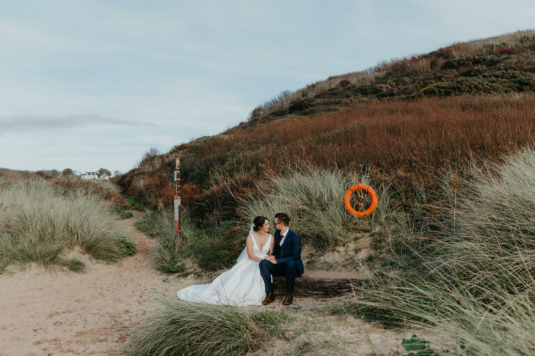 Beautiful portrait of bride and groom sitting at the beach following their wedding ceremony at Manorbier Castle, near Tenby on the Pembrokeshire Coast